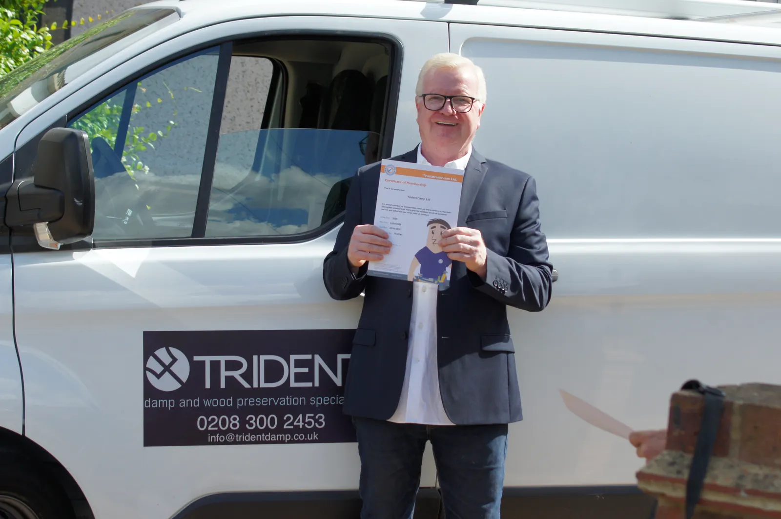 Joseph O'Regan holding a Trident Damp guarantee document beside the company van