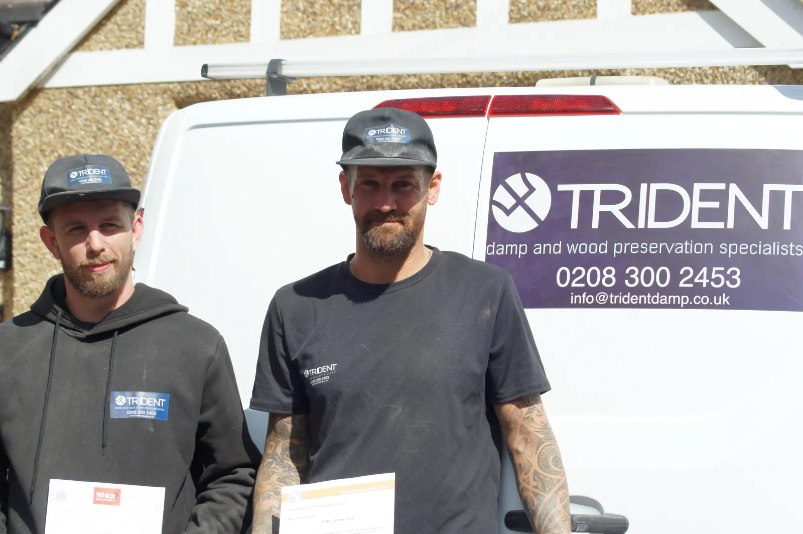 Two Trident Damp team leaders in company workwear holding their review certificates